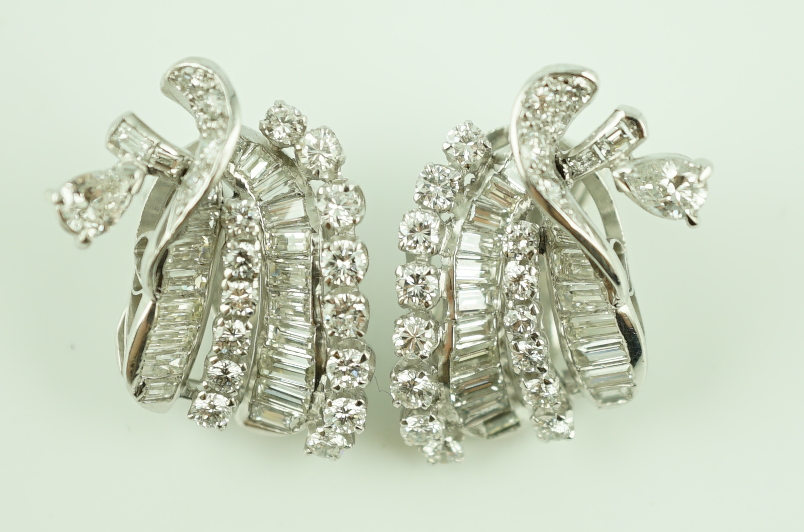 A pair of platinum and round cut, baguette cut and pear cut diamond cluster set scrolling ear clips